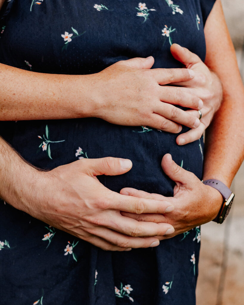 Babybauch Fotoshooting bei Ansbach – Hände eines Paares liegen liebevoll auf dem Babybauch