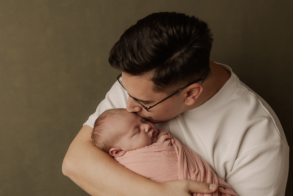 Neugeborenenfotografie Ansbach – Vater küsst sein schlafendes Baby liebevoll im Arm, natürliche Familienfotografie