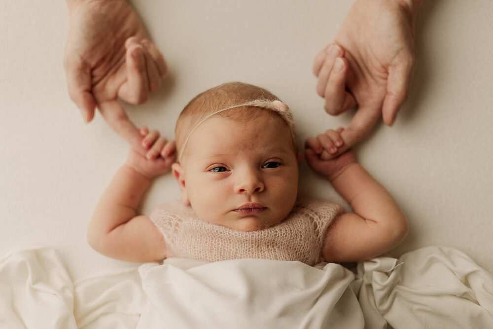 Neugeborenenfotografie Ansbach – Baby liegt entspannt und hält die Finger der Eltern, natürliche Newbornfotografie zuhause