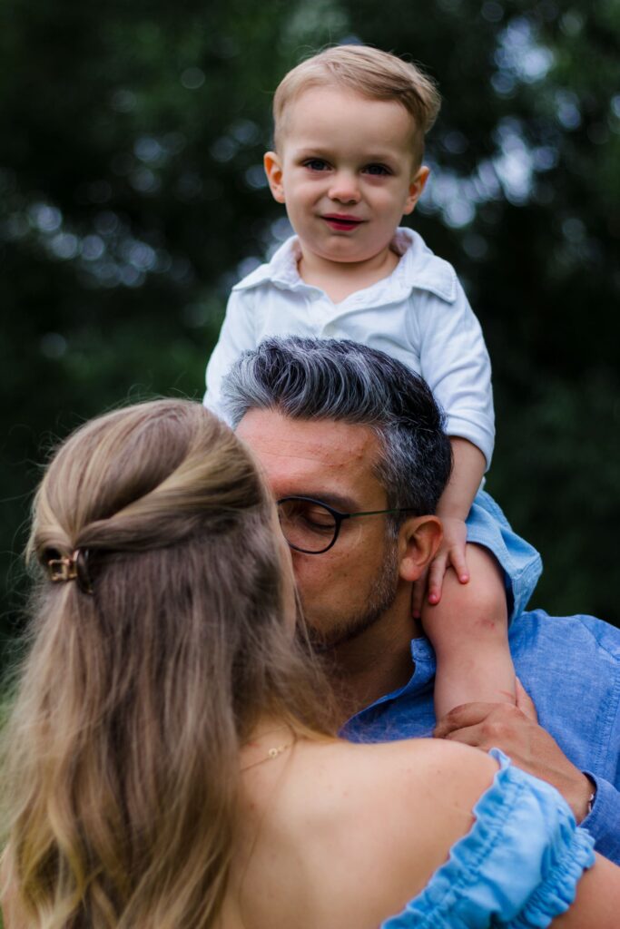 Eltern küssen sich liebevoll, während ihr Kind auf den Schultern sitzt – natürliches Familienshooting im Landkreis Ansbach