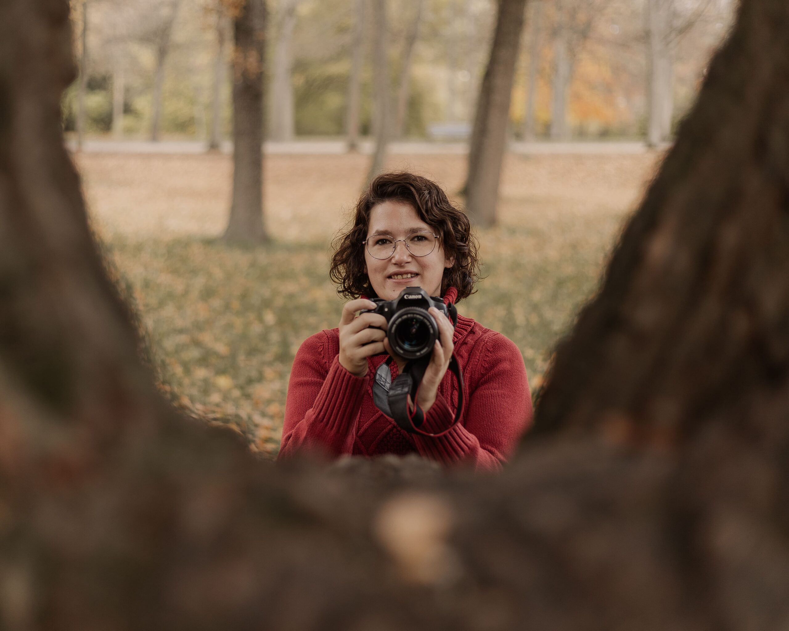 Familienfotografin Sandra von Matelis Fotografie mit Kamera zwischen zwei Baumstämmen im herbstlichen Park