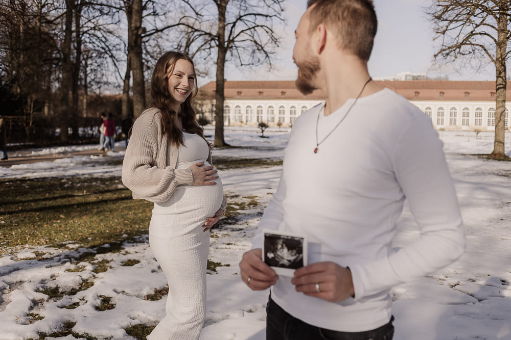 Babybauch Fotoshooting im Freien bei Ansbach – Paar lacht gemeinsam, Ultraschallbild in der Hand