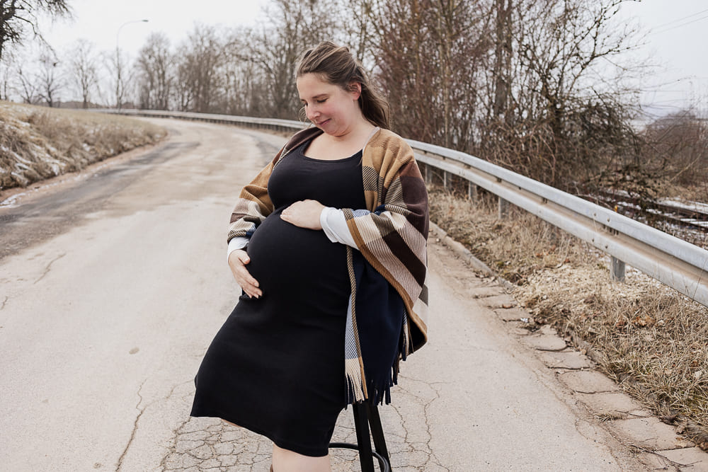 Babybauch Fotoshooting bei Ansbach – schwangere Frau sitzt entspannt auf einer Straße und hält ihren Bauch