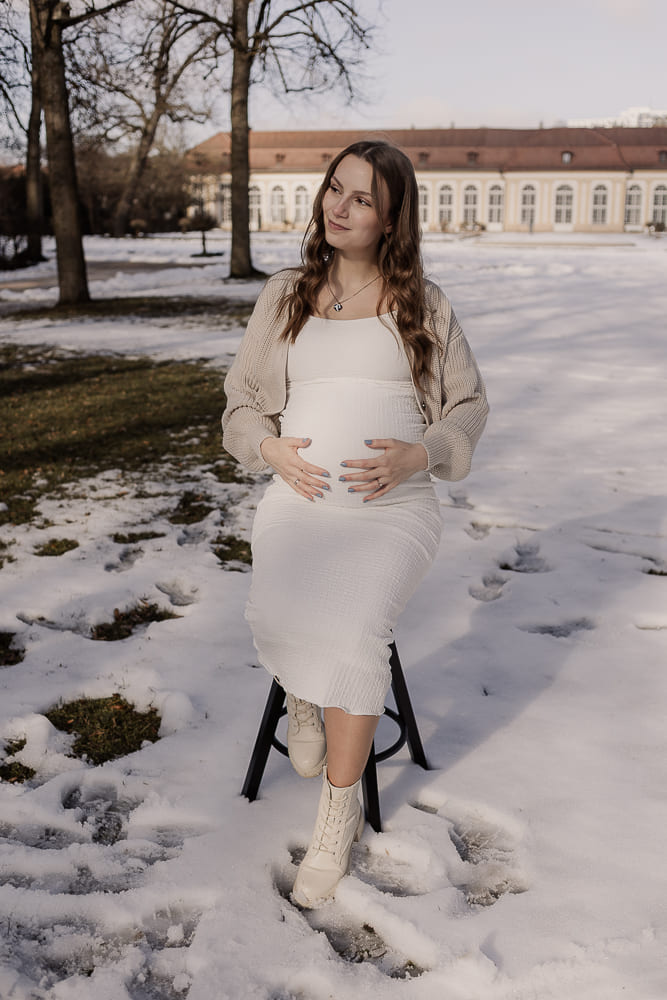 Babybauch Fotoshooting im Freien bei Ansbach – schwangere Frau sitzt im Schnee und hält ihren Bauch