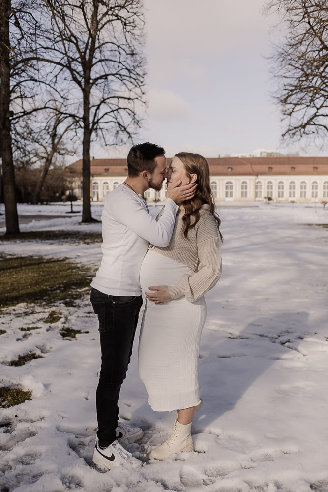 Babybauch Fotoshooting im Freien bei Ansbach – Paar küsst sich liebevoll im Schnee während Schwangerschaft